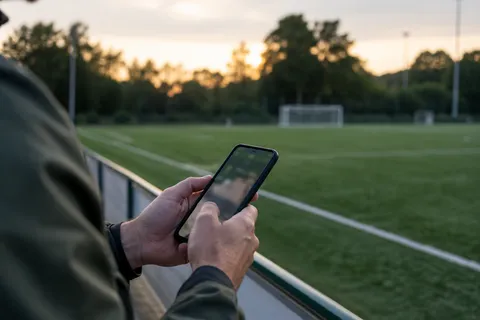 AI illustration: Phone held beside an empty football field